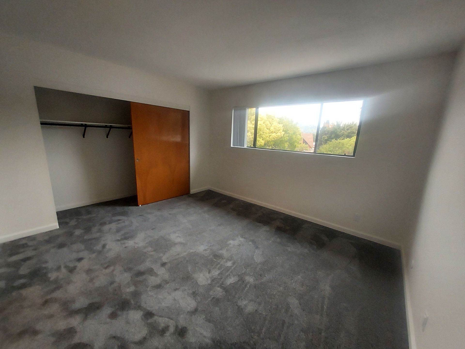 An empty bedroom with a large window and a closet.