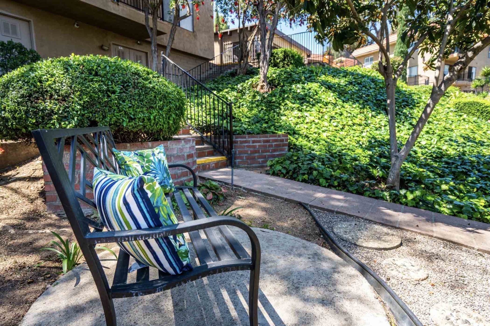 A bench with a striped pillow on it is sitting on a concrete patio.