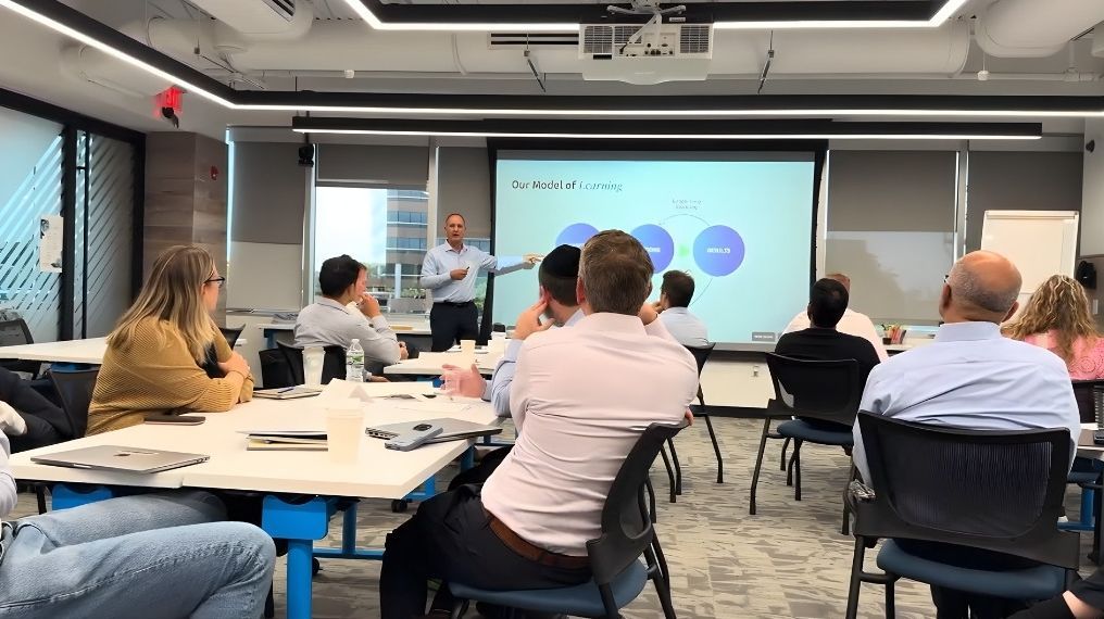 Man presenting to a group in a modern office, pointing at a projected diagram.