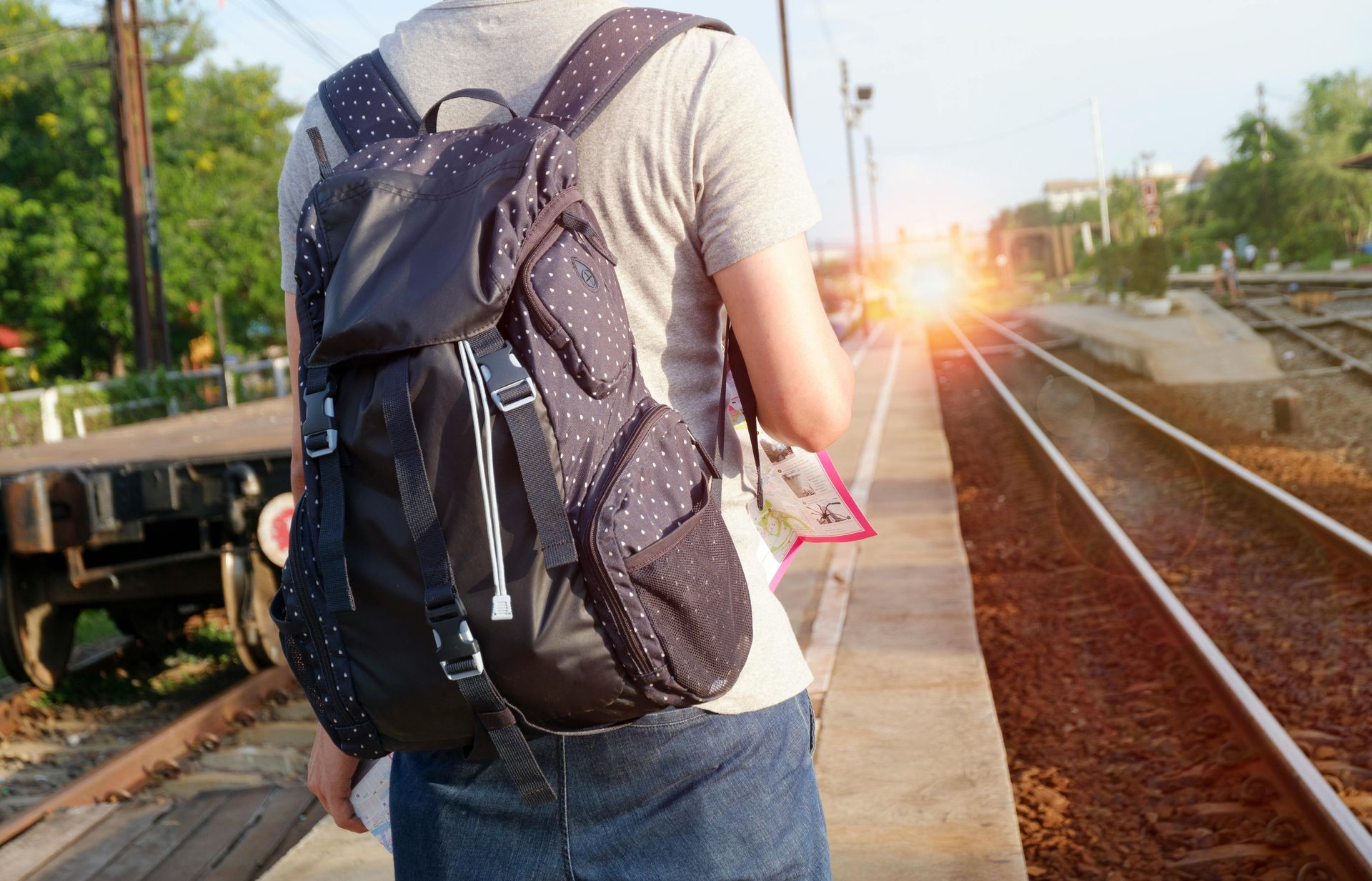 Person with backpack stands on train platform, watching approaching train.