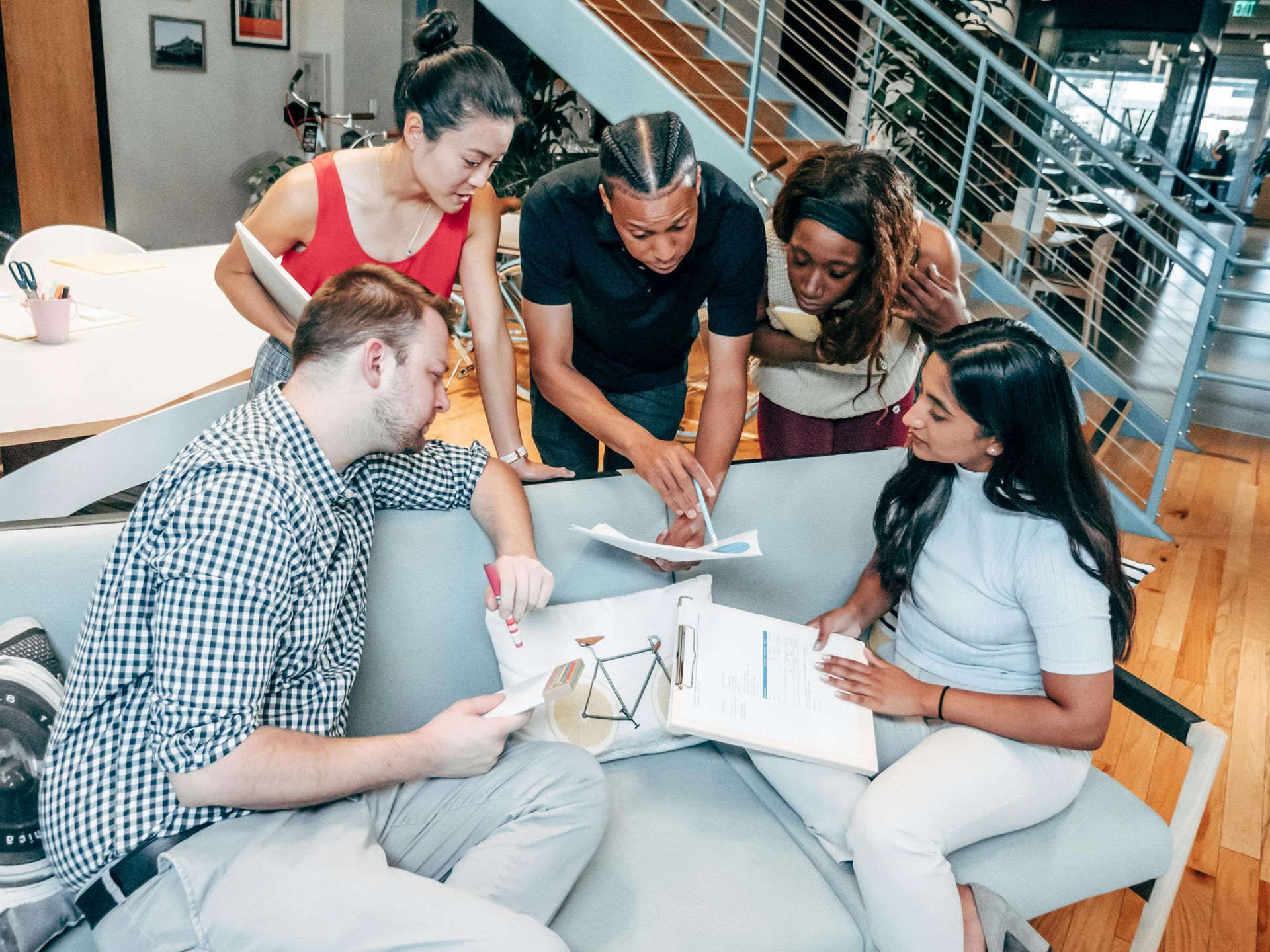 Group of people collaborating over papers on a couch in an office; they are examining charts and discussing.