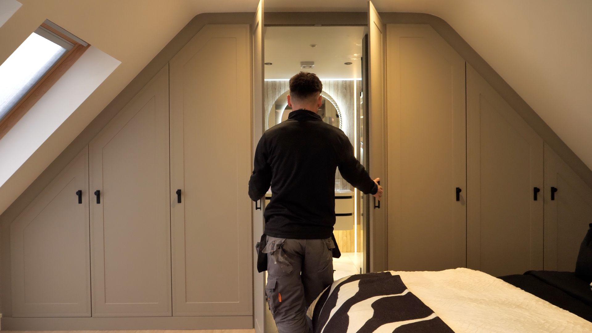 Person opening a closet door in an attic bedroom. Neutral walls, dark hardware, and a zebra-print blanket are visible.