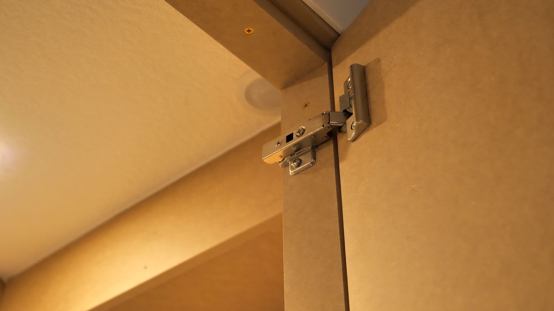 Hinges mounted on a tan-colored door frame, near a ceiling.