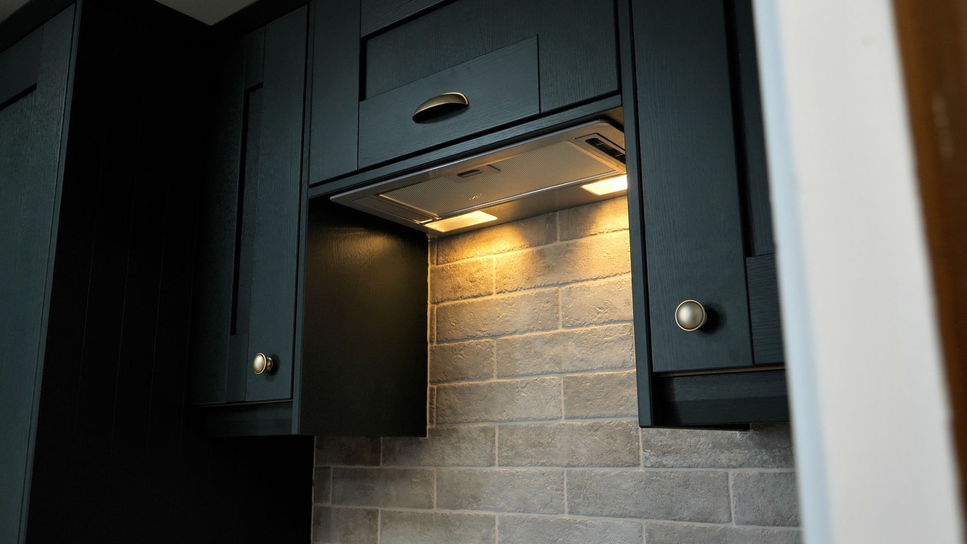 Dark blue kitchen cabinets with range hood and tiled backsplash.