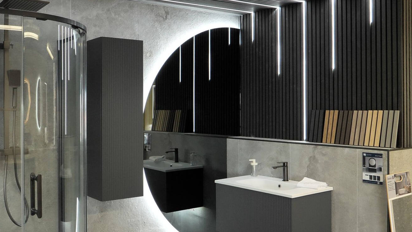 Modern bathroom with a round backlit mirror, dark gray cabinets, and a glass shower.