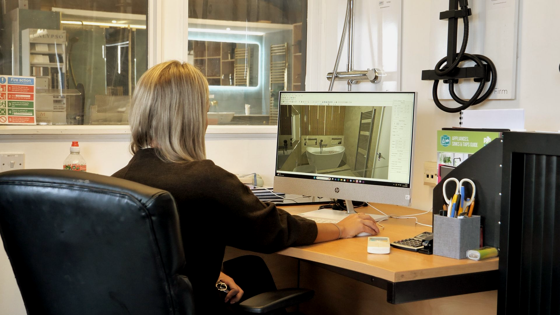 Woman at a desk with a computer, looking at the screen. Office setting with scissors and a pen holder.