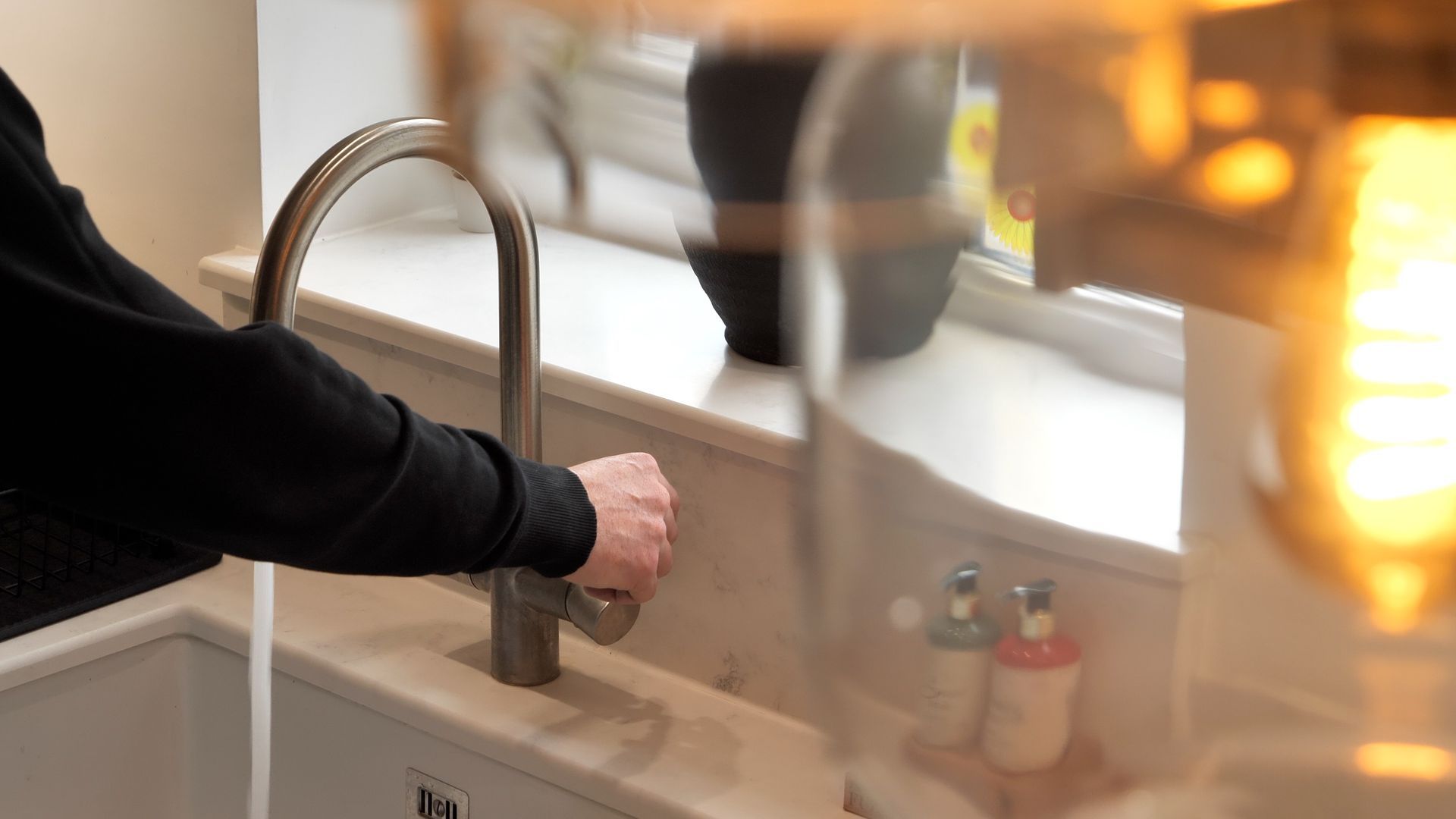 Person turning on a faucet in a kitchen sink. The faucet is silver.