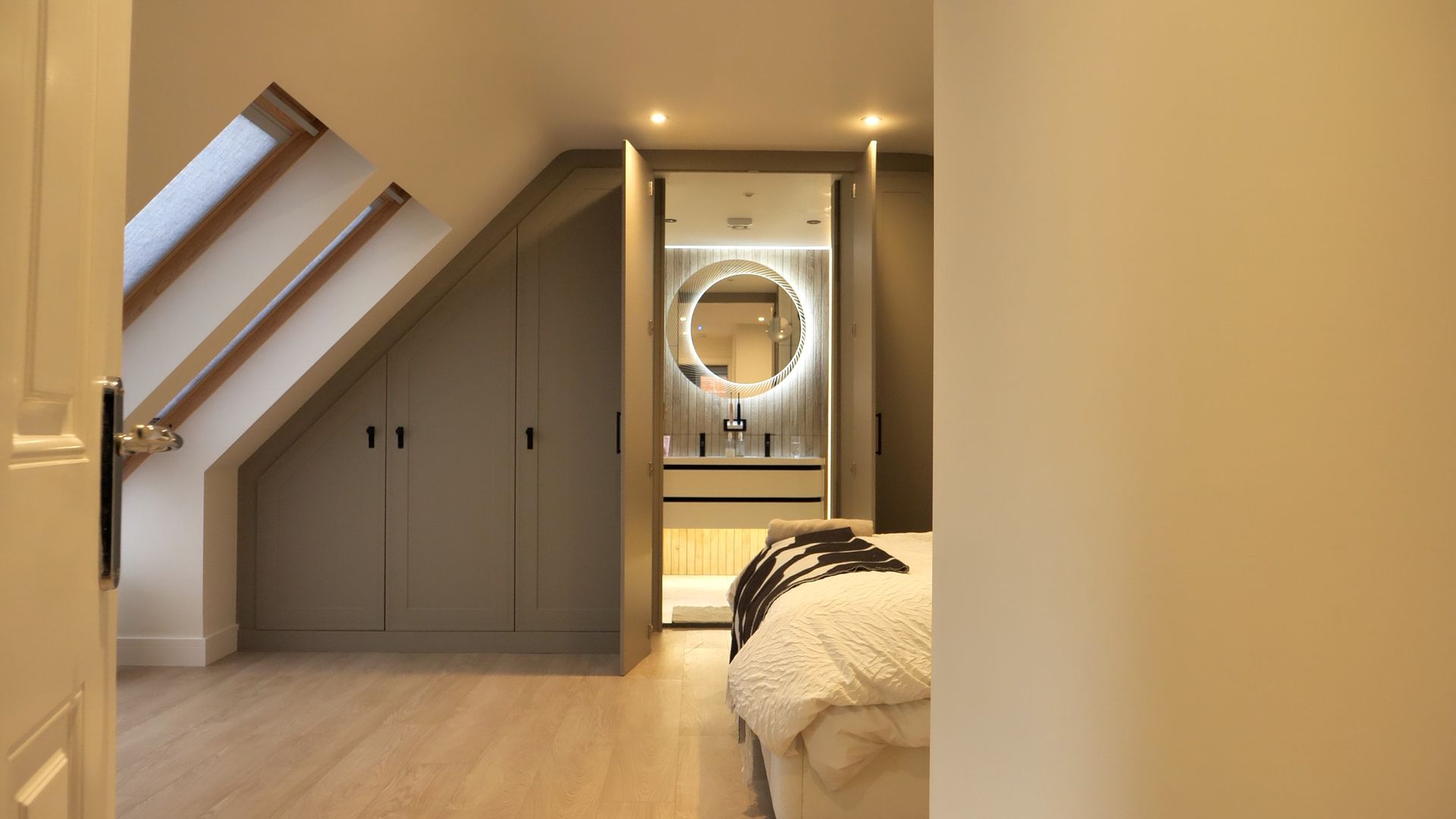 Modern bedroom with sloped ceiling, built-in storage, and vanity with illuminated mirror.