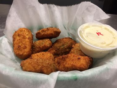 A basket of fried pickles with a dipping sauce on a table.