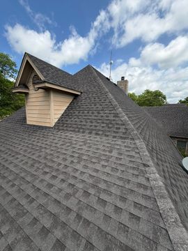 Steep gray shingled roof with a dormer and chimney under a cloudy sky