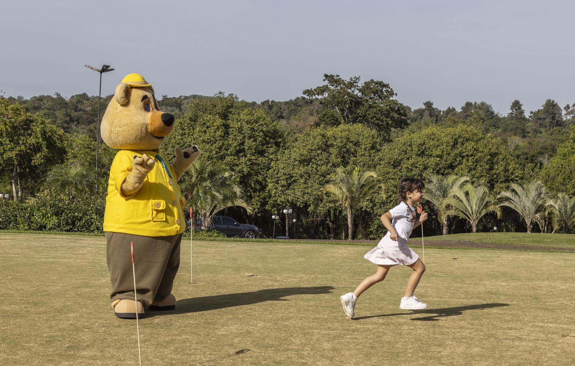 Uma menina está correndo em um campo ao lado de um mascote.