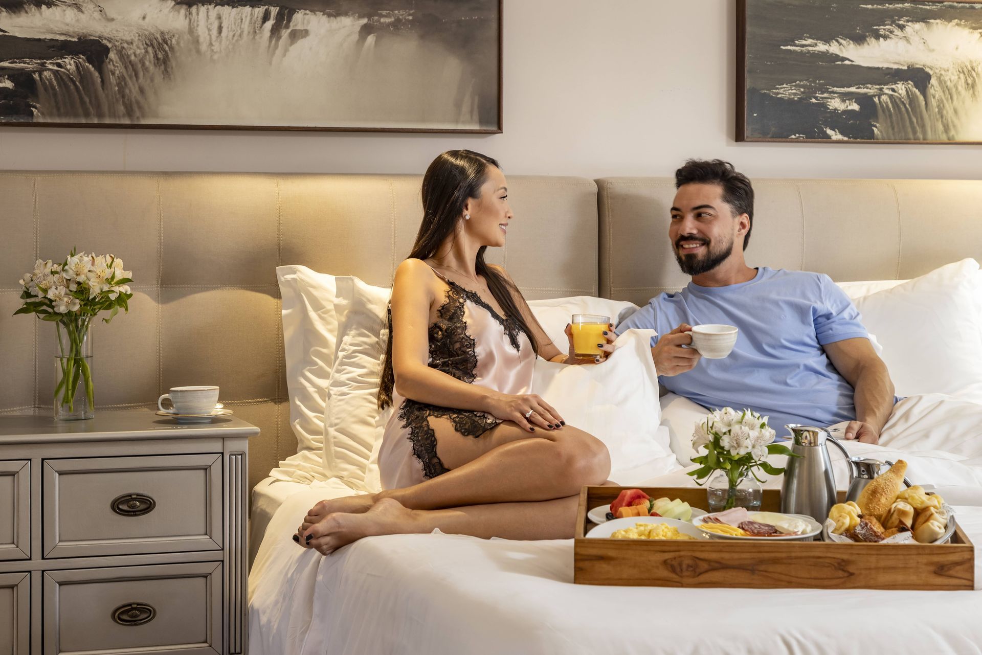 Um homem e uma mulher estão sentados em uma cama com uma bandeja de comida.