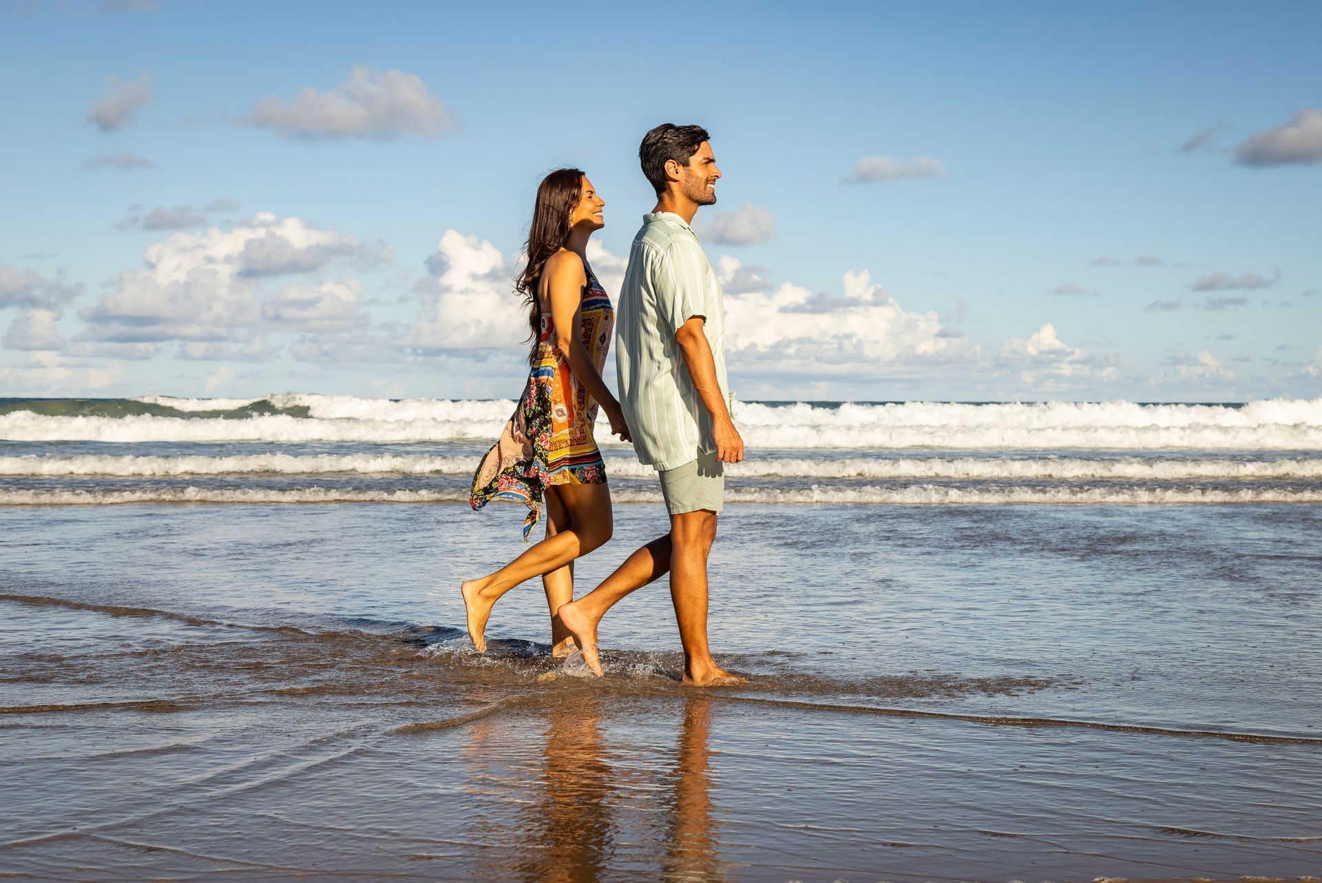 A man and a woman are walking on the beach holding hands.