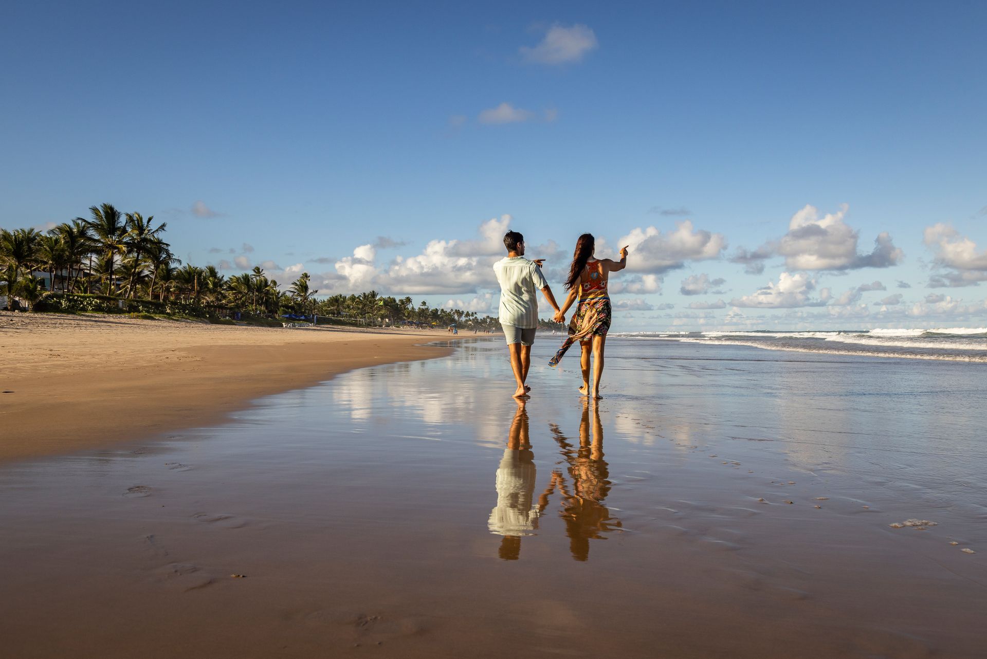 Um homem e uma mulher estão caminhando na praia de mãos dadas.
