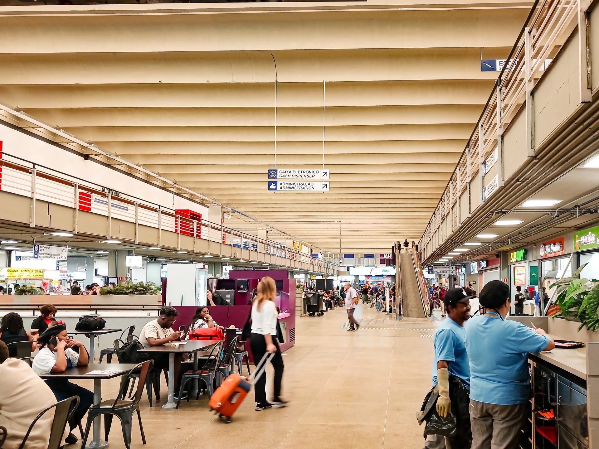 Busy airport terminal with travelers sitting, walking, and waiting near shops and gates
