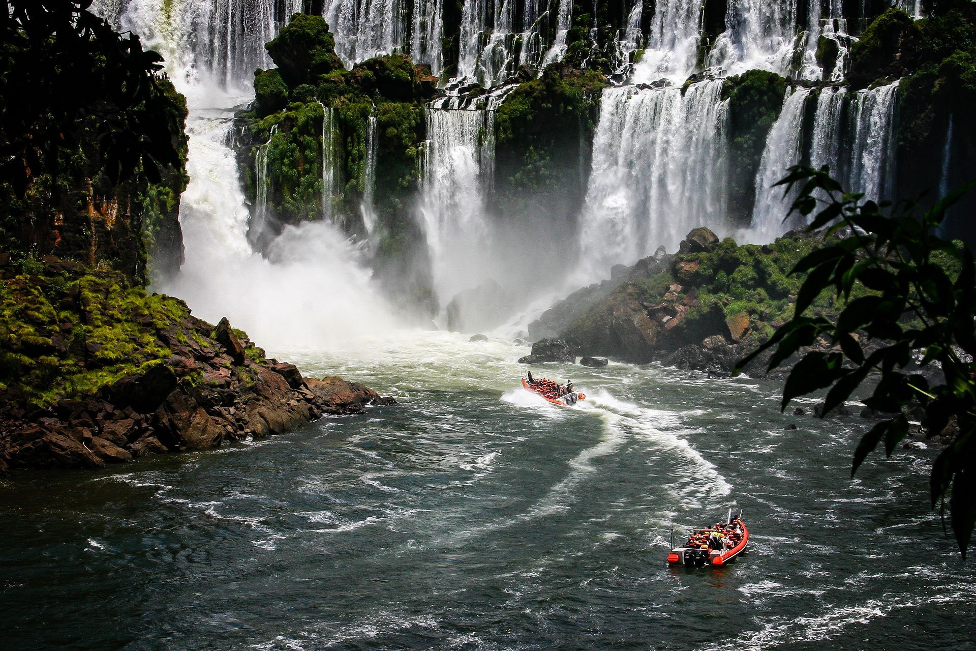 A boat is going down a river in front of a waterfall.