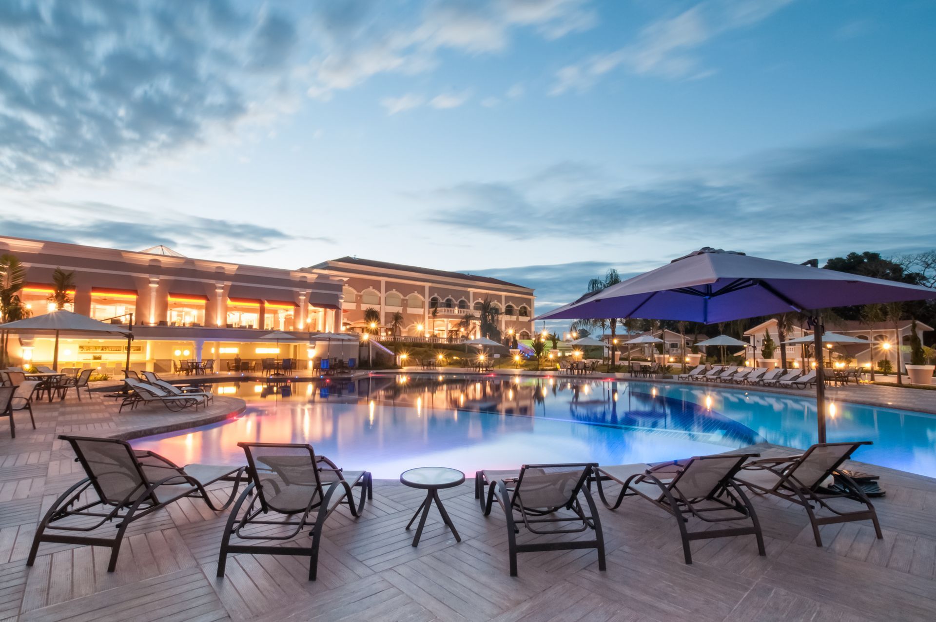 Swimming pool with lounge chairs, umbrella, and a building at dusk. Reflections in the water.