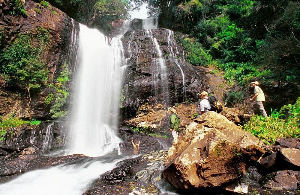 Two people are sitting on rocks in front of a waterfall.