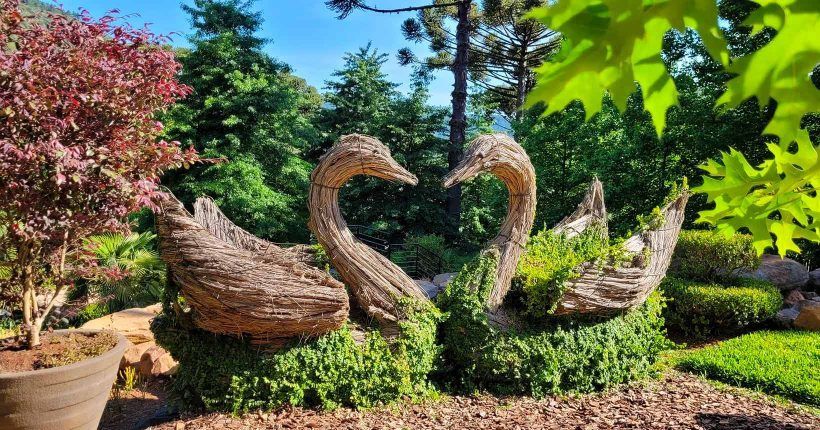 A couple of swans made of straw are standing next to each other in a garden.