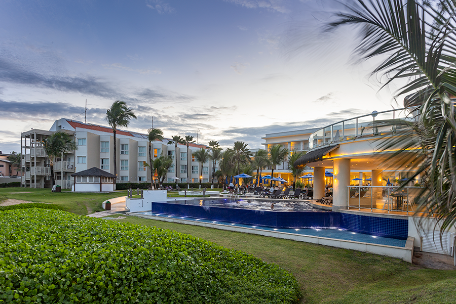 Resort pool and buildings at dusk, green grass, palm trees.