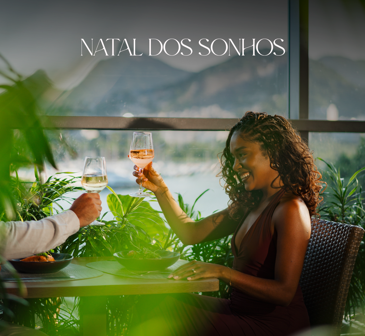 Duas pessoas brindando em uma mesa de jantar festiva com a inscrição “Natal dos Sonhos” acima delas.