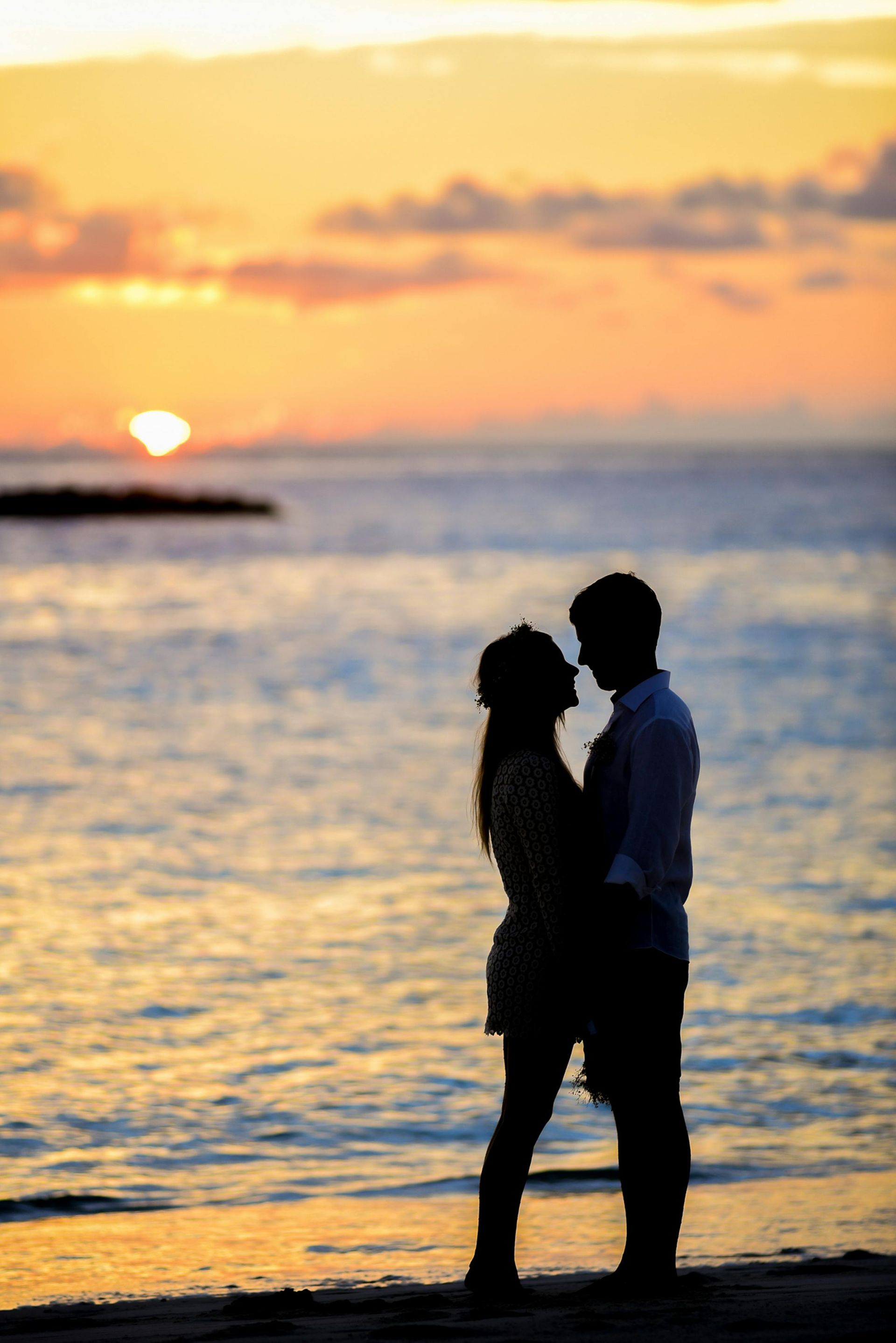 Couple silhouetted on beach at sunset, embracing with ocean backdrop.