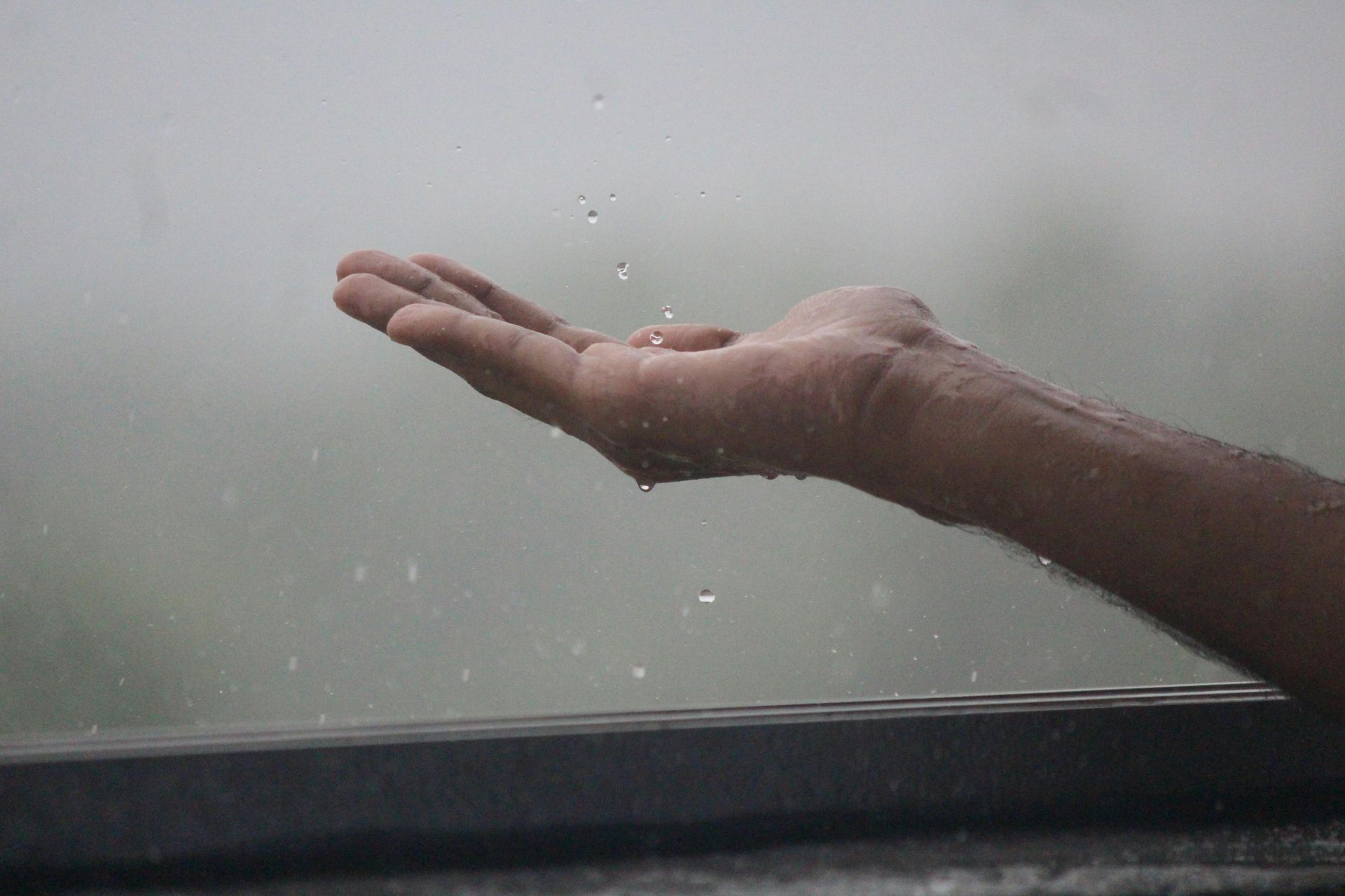 Hand outstretched, catching raindrops outdoors, grey sky.