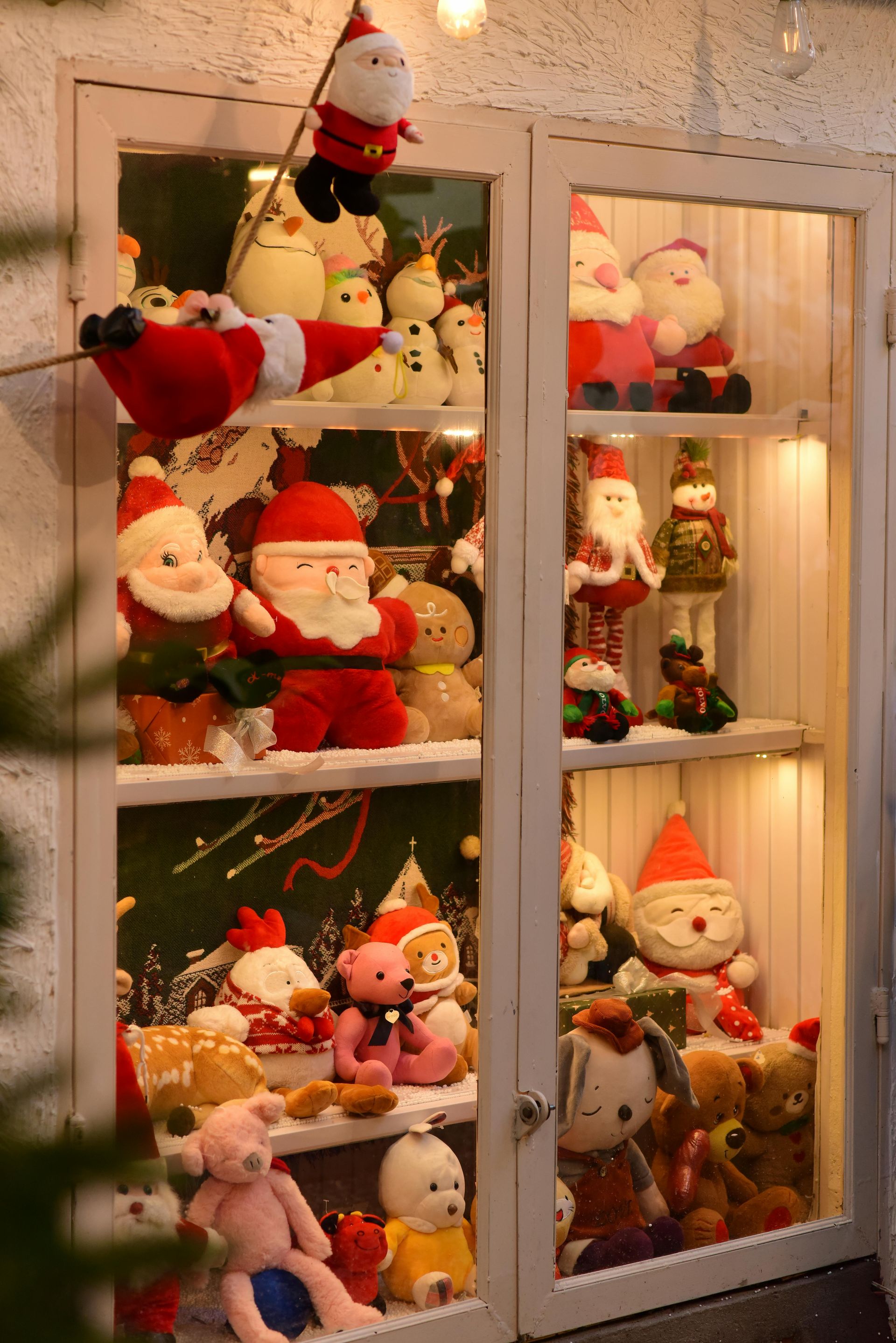 Christmas display cabinet, stuffed Santa Clauses, snowmen, and bears on shelves, illuminated.