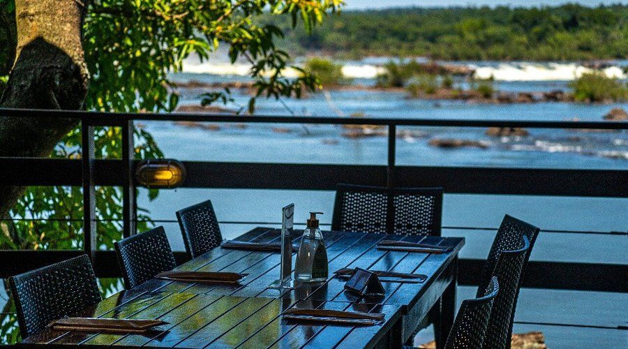 Outdoor dining table set for a meal with a river and trees in the background.