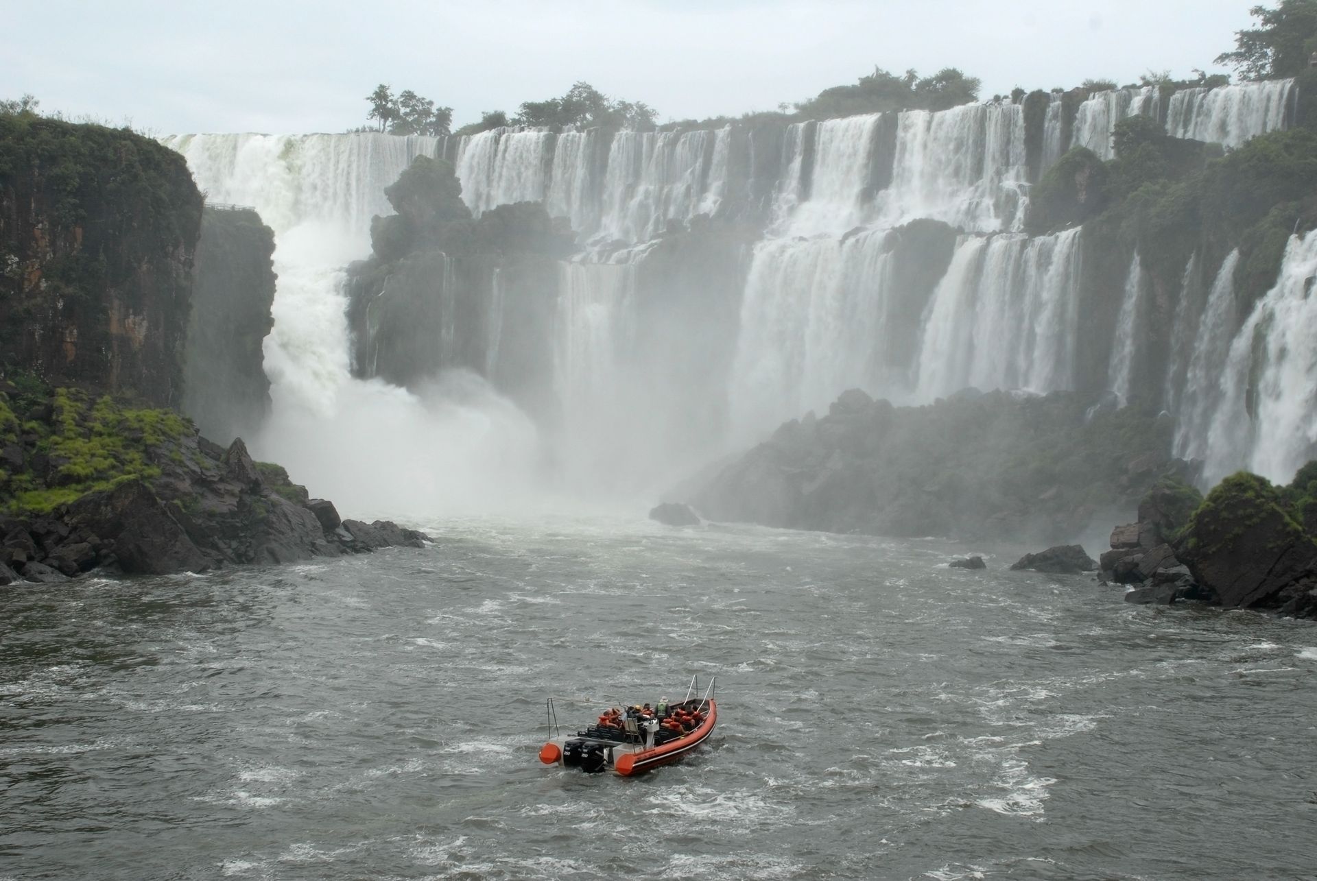 Um barco está flutuando rio abaixo em frente a uma cachoeira.