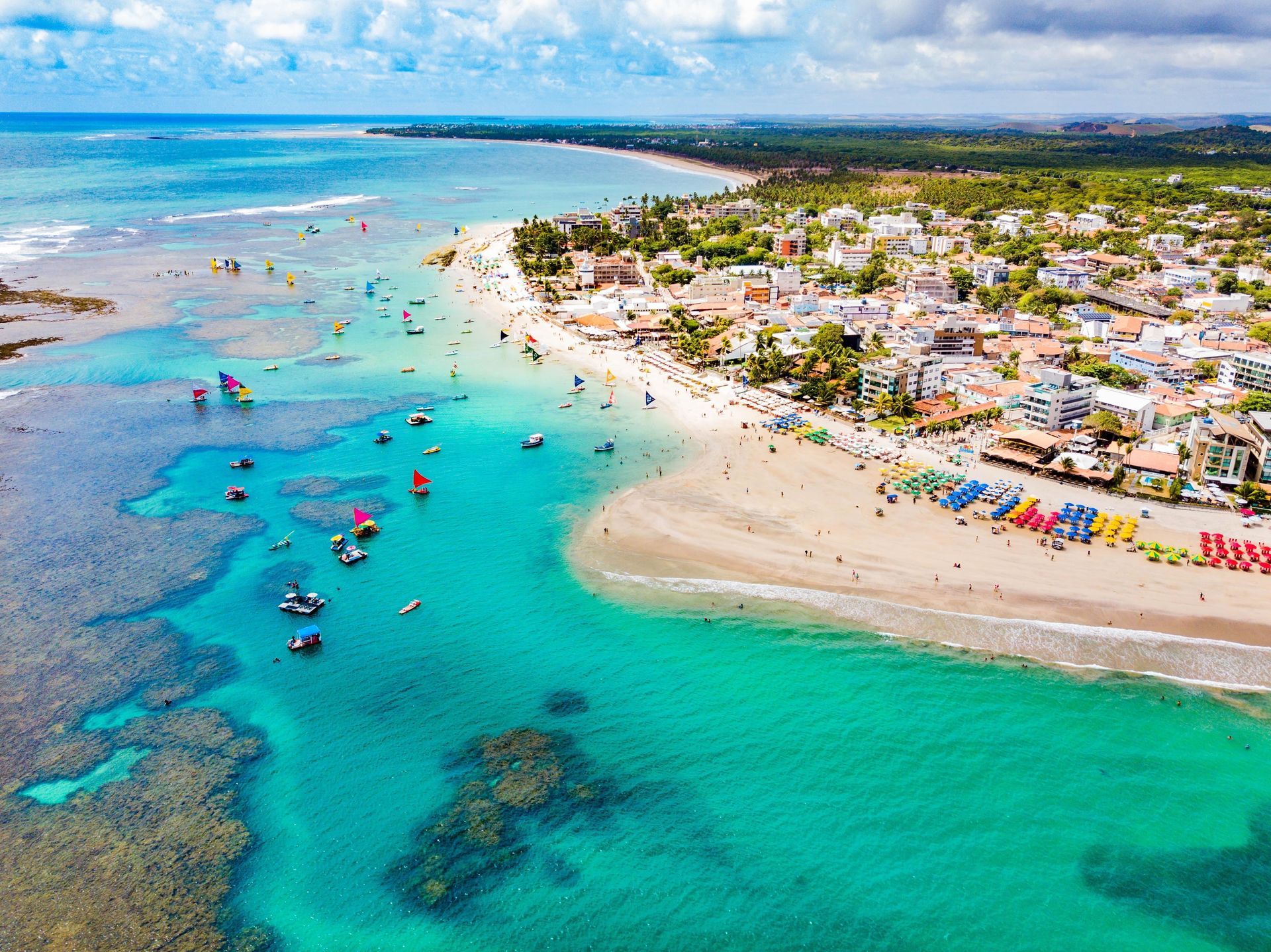Uma vista aérea de uma praia com barcos na água e uma cidade ao fundo.
