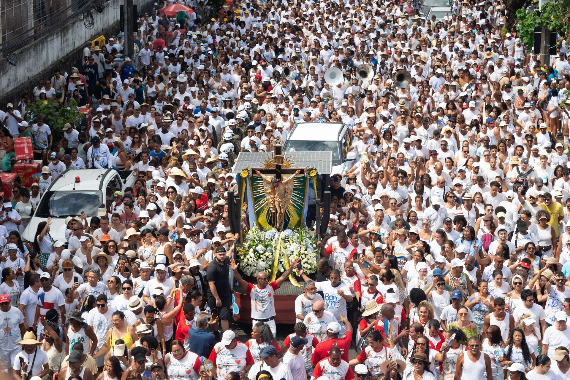 Uma grande multidão de pessoas está caminhando pela rua carregando uma estátua de Jesus na cruz.