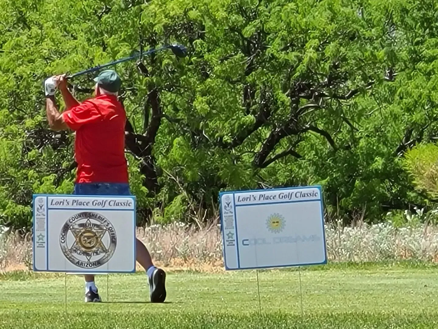 A man in a red shirt is swinging a golf club on a golf course