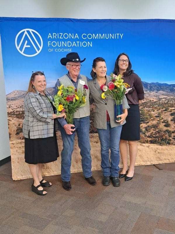A group of people standing in front of an arizona community foundation banner holding flowers.