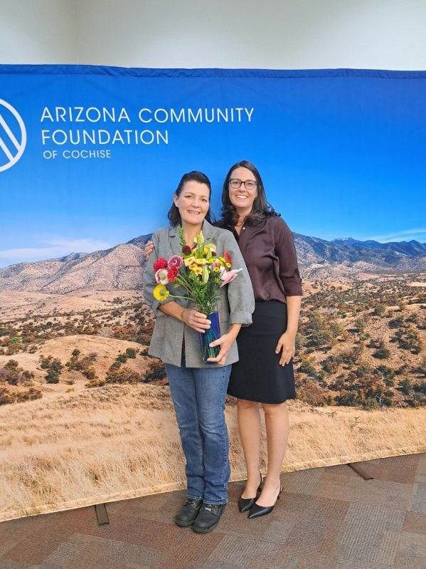 Two women are standing next to each other in front of an arizona community foundation sign.