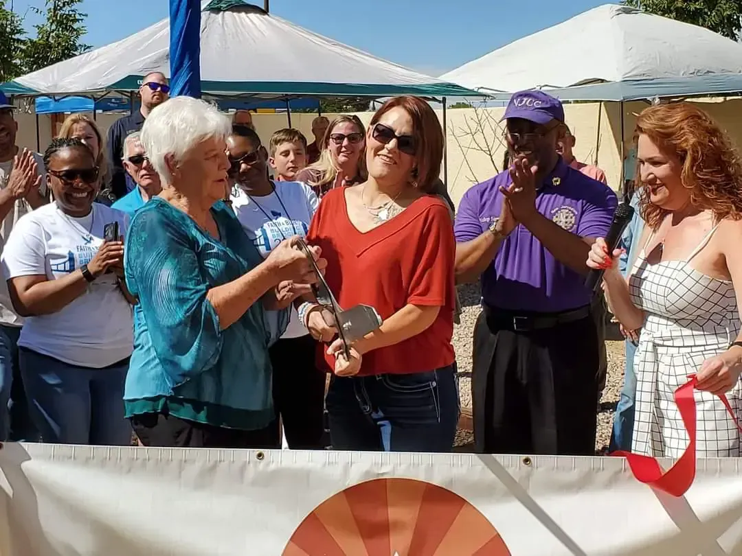 A group of people are standing around a white banner with a red ribbon.