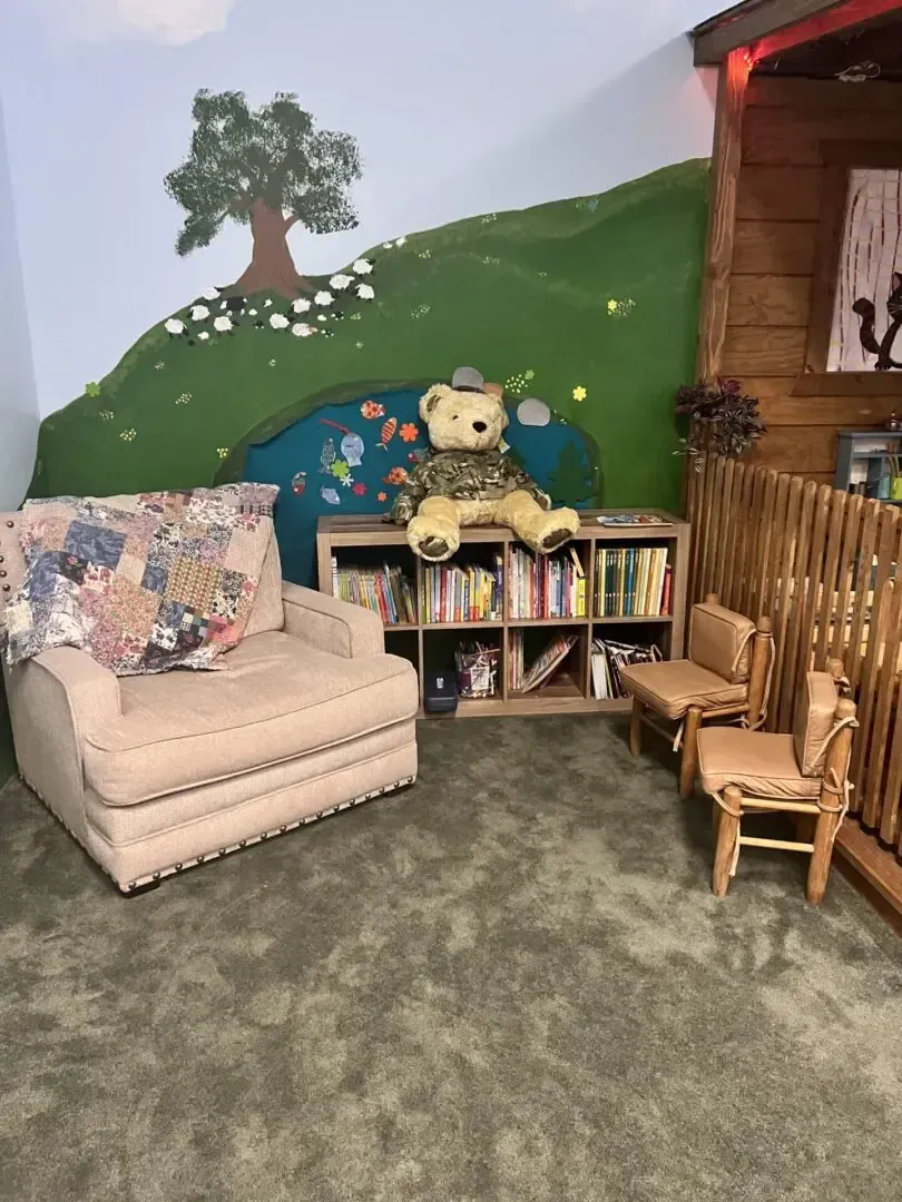A teddy bear is sitting on a bookshelf in a room with chairs.