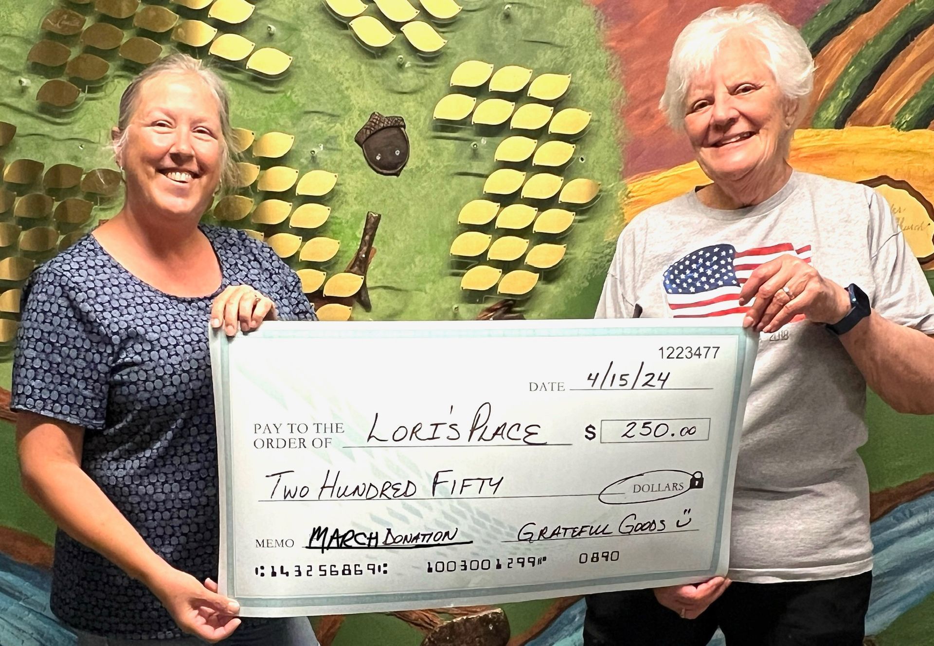 Two women are holding a large check in front of a mural.