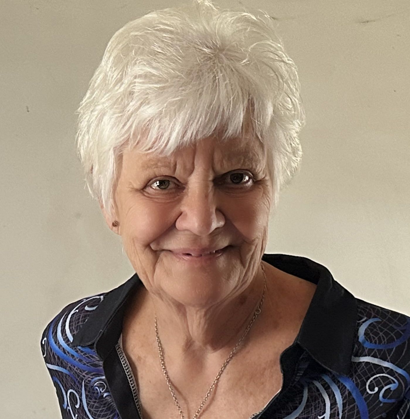 A woman with white hair is wearing a jacket and a necklace.