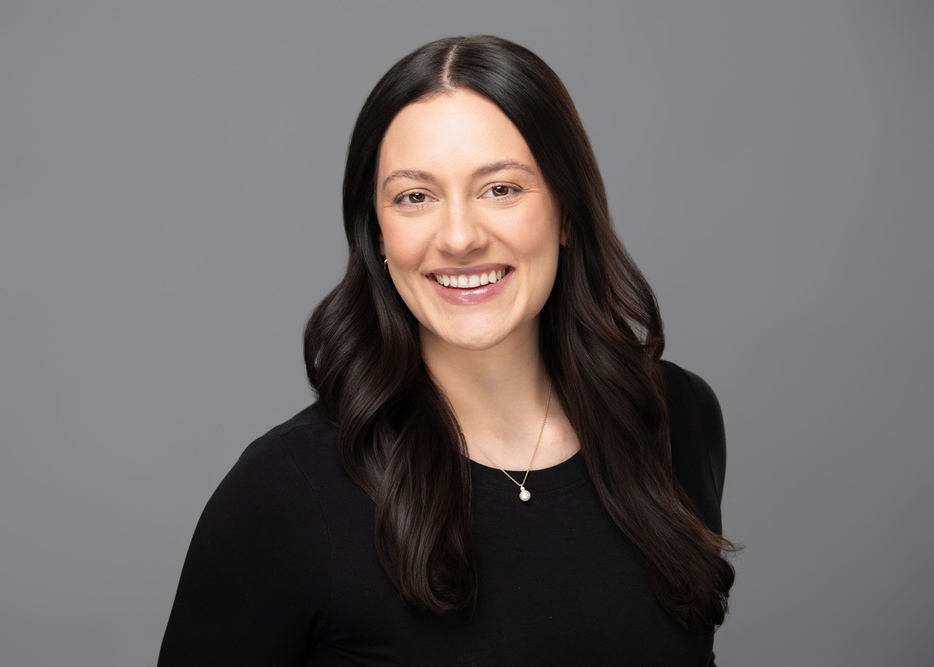 A woman in a hat is kneeling down and hugging a brown dog.