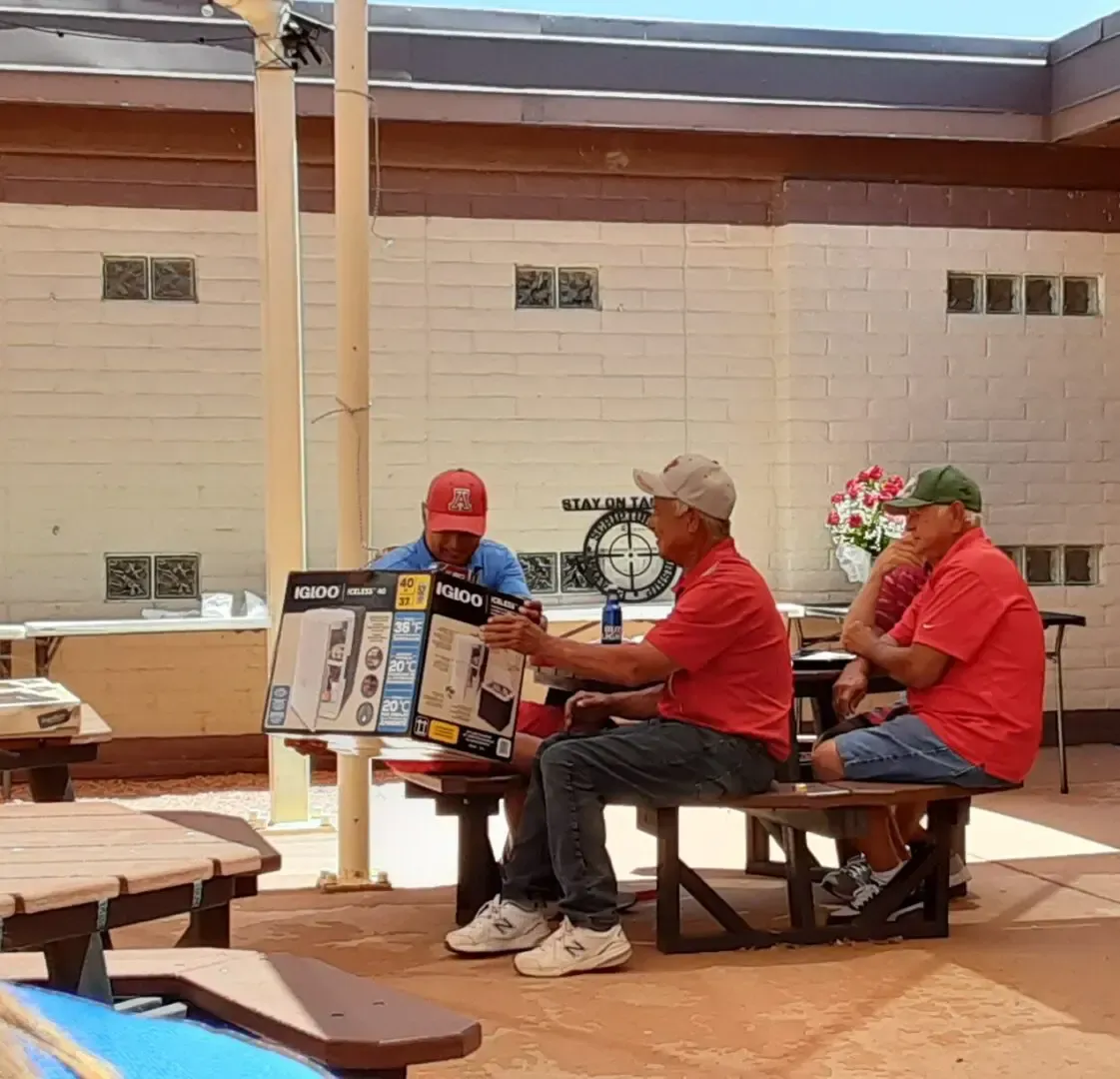 A group of men are sitting at a picnic table holding a box.