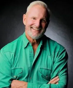 A man with a beard is wearing a green shirt and smiling.
