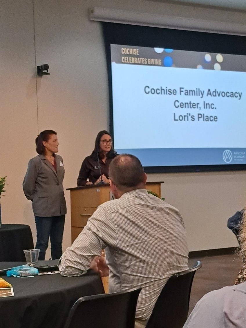 A group of people are sitting at tables in front of a screen that says cochise family advocacy center inc.