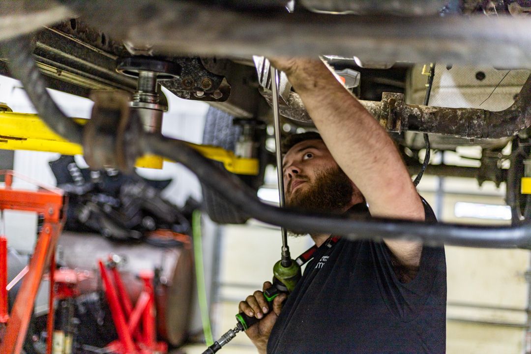 Mechanic Tightening Bolt Underneath Vehicle on Lift | Tex's Transmissions Complete Auto & Truck Care
