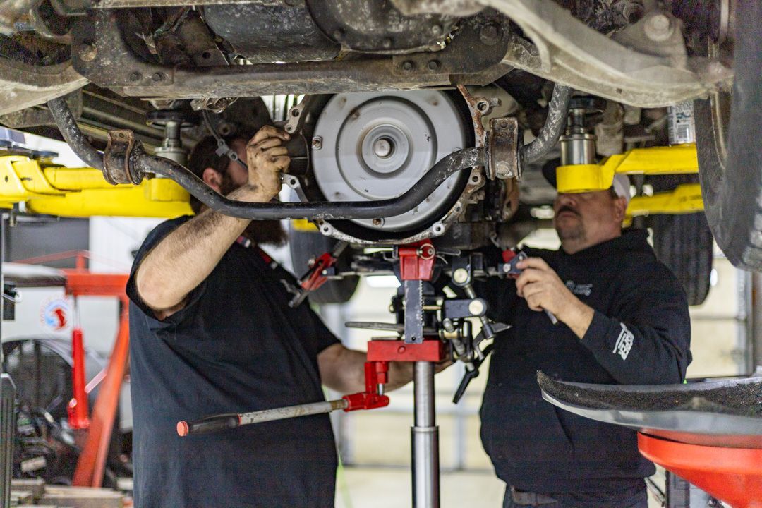 Two Technicians Installing Transmission Under Vehicle on Lift | Tex's Transmissions Complete Auto & Truck Care