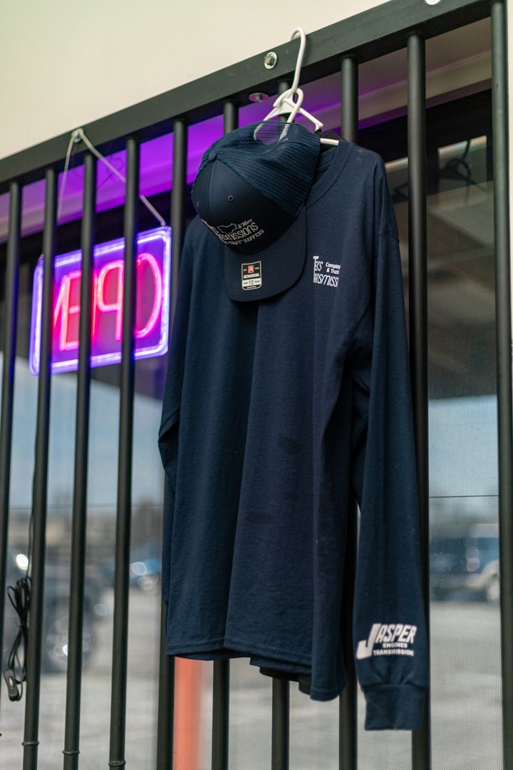 Tex’s Transmissions Branded Shirt Hanging by Neon Open Sign | Tex's Transmissions Complete Auto & Truck Care