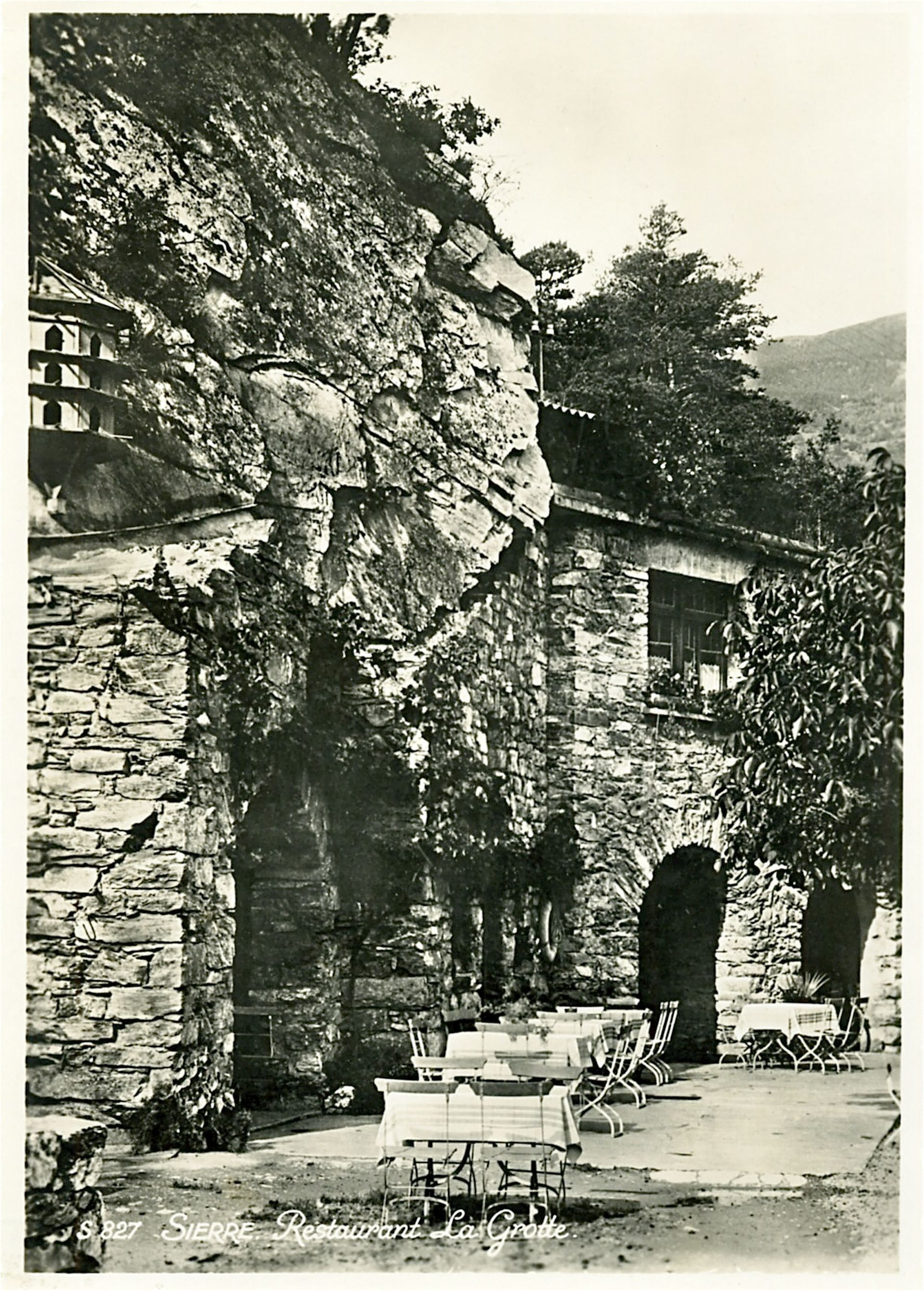 Une photo en noir et blanc d’un bâtiment en pierre avec des tables et des chaises devant