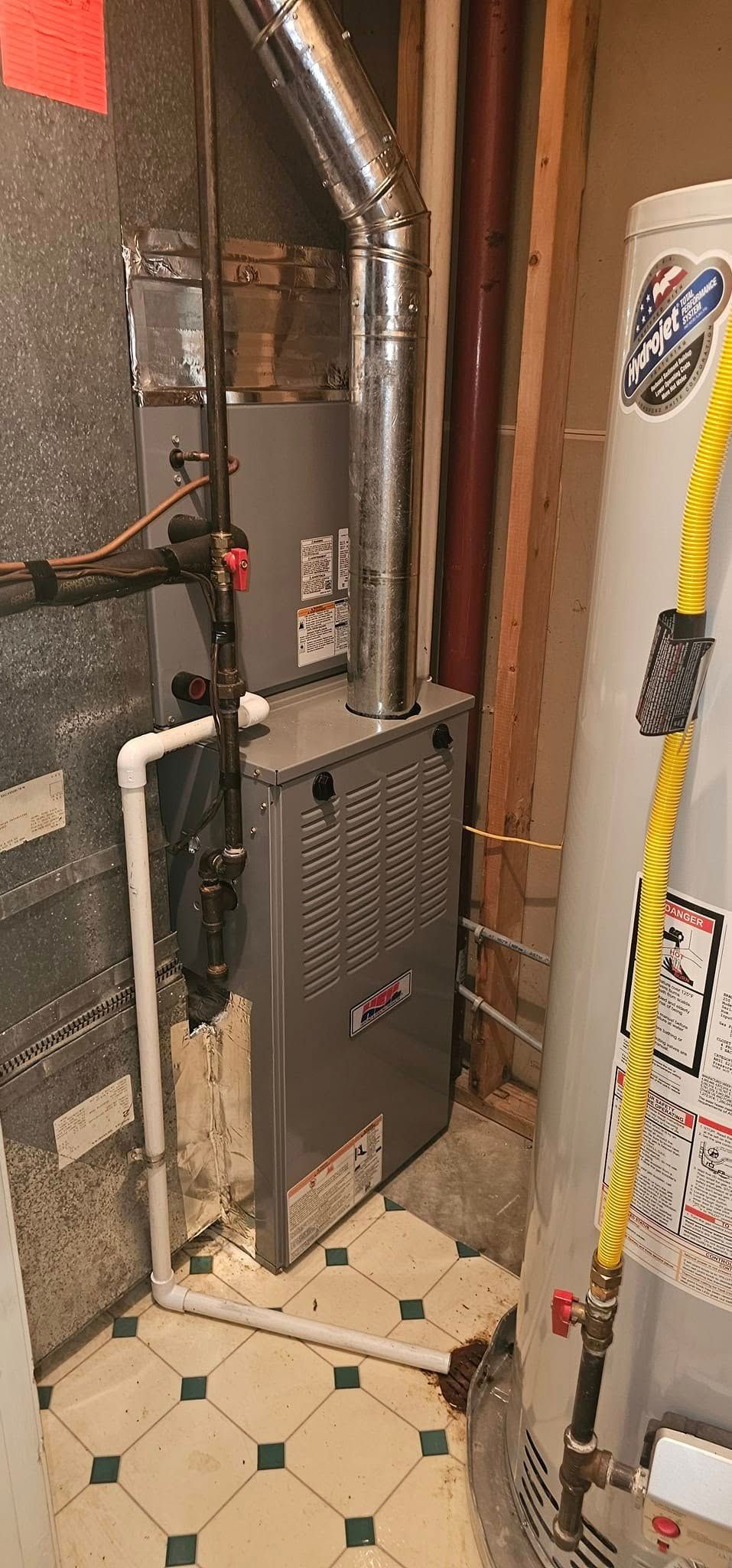 Basement utility area with furnace, pipes, ductwork, and tiled floor.