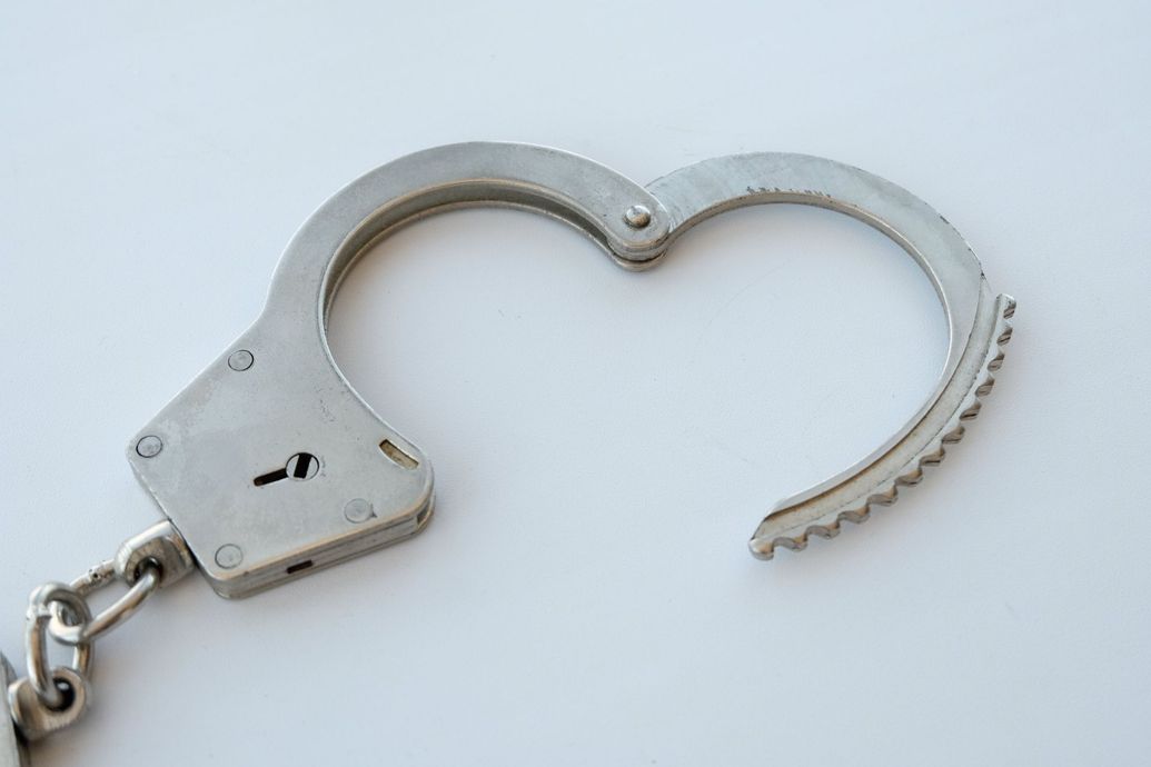 A close-up of a metal handcuff in an open position against a plain white background.