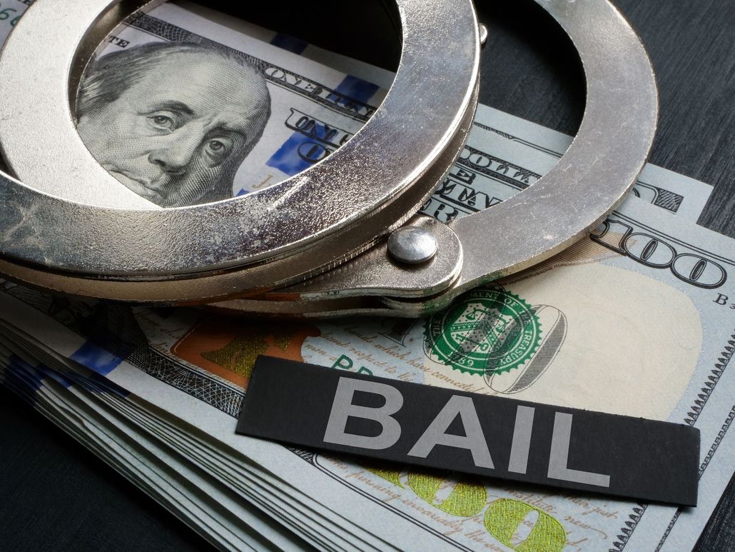 Metal handcuffs resting on a stack of US hundred-dollar bills with a black sign labeled 